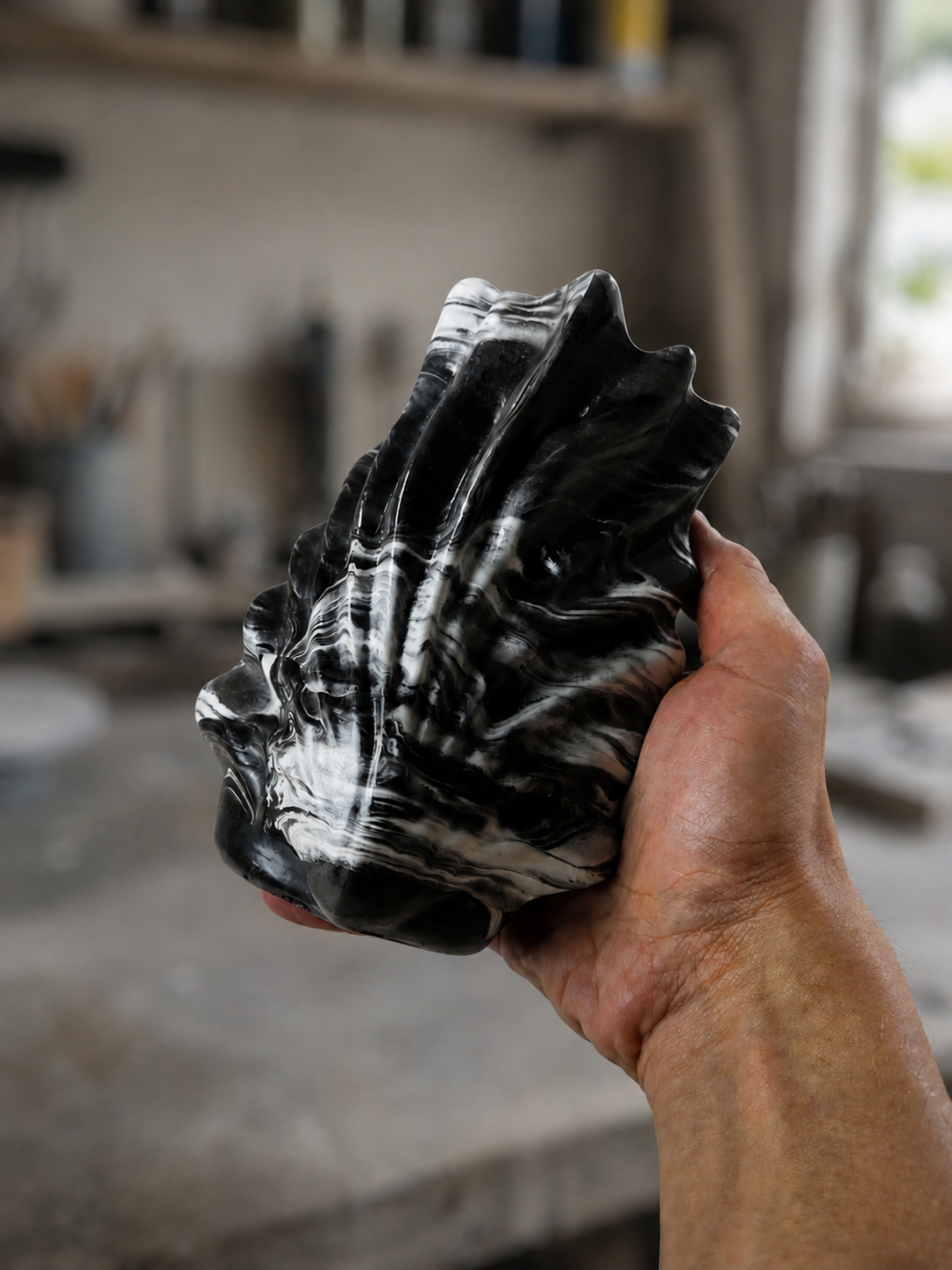 A finished black-and-white marbled shell object held in hand before packaging